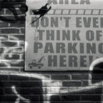 B&W 35mm photo of a graffiti covered wall with a sign reading "DON'T EVEN THINK OF PARKING HERE"