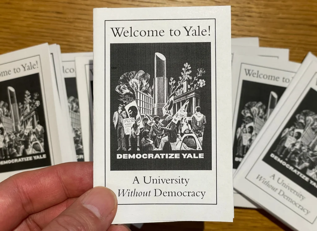 Hand holding a zine that says "Welcome to Yale! A University Without Democracy." The image on the cover shows protestors from various generations of Yale students standing in front of the iconic lipstick sculpture that used to stand in Yale's Beineke Plaza. Words "Democratize Yale" under the graphic.