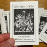 Hand holding a zine that says "Welcome to Yale! A University Without Democracy." The image on the cover shows protestors from various generations of Yale students standing in front of the iconic lipstick sculpture that used to stand in Yale's Beineke Plaza. Words "Democratize Yale" under the graphic.